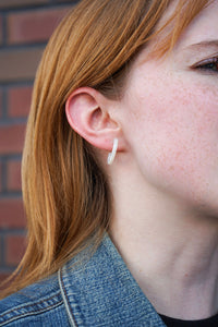 Close-up of a person wearing a hoop earring with a blurred brick wall background